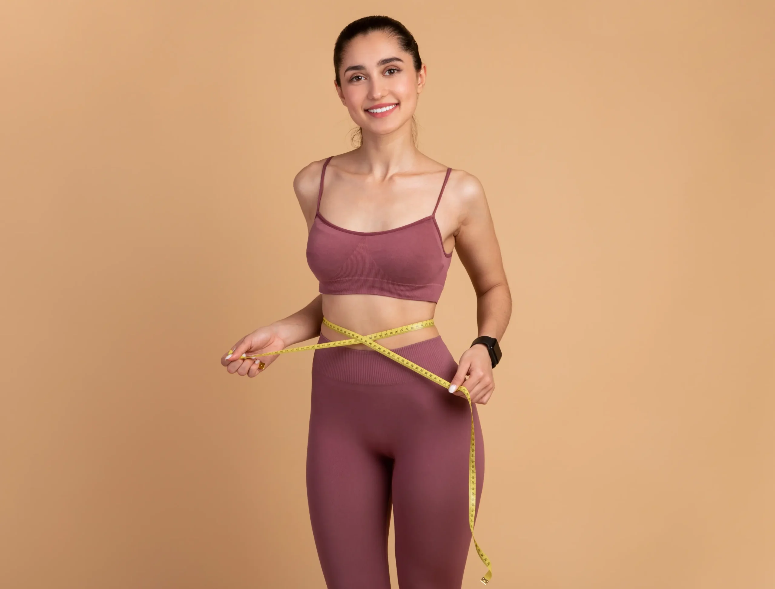 Woman in gym clothes holding tape measure on waist